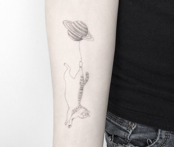 Cat tattoo featuring a floating cat holding a Saturn balloon on a person's forearm.