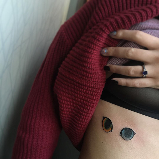 Two colorful cat eyes tattooed on a person's side, partially covered by a red sweater.