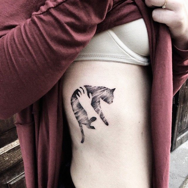 Cat tattoo on person's rib, showcasing a minimalist design under a red shirt.