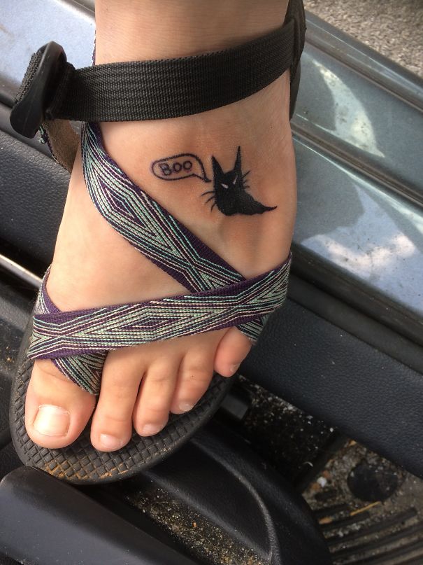Foot with a small black cat tattoo saying "boo," showcasing cat tattoo design.