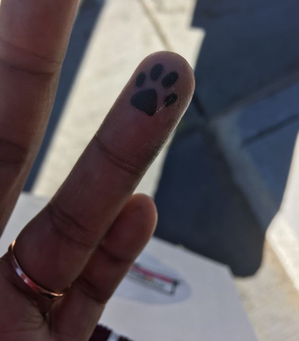 Finger with a small cat tattoo of a paw print, symbolizing self-expression for a cat person.