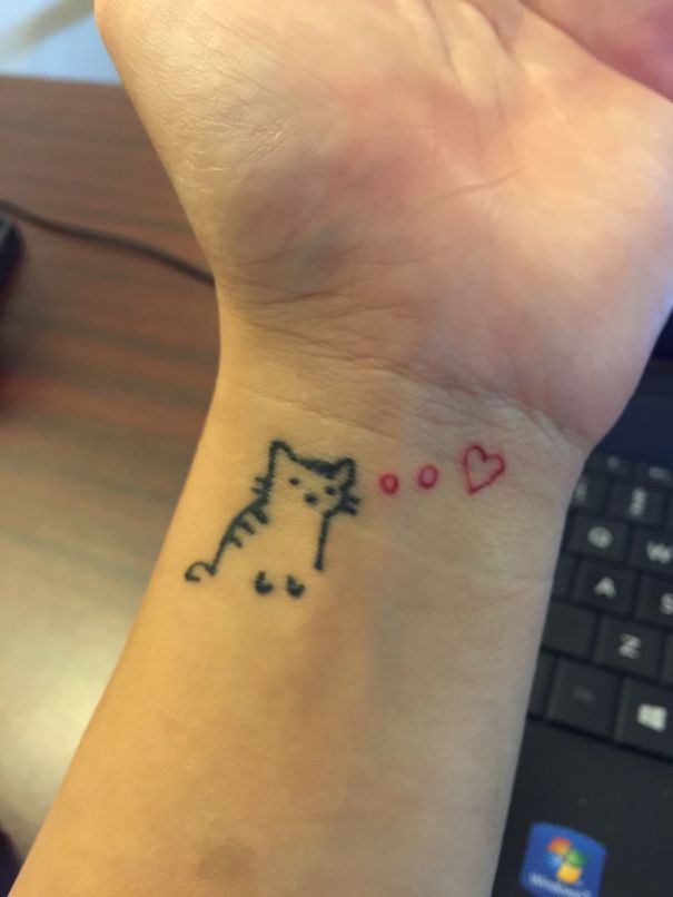 Cat tattoo on wrist, featuring a simple cat design with a heart, expressing love for cats.