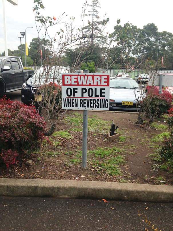 Picture with cars and sign that says beware of pole when reversing