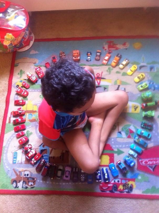 Child arranging toy cars in a perfect circle on a colorful mat, satisfying a perfectionist's love for symmetry.