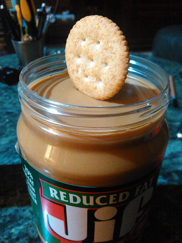 Cracker perfectly balanced on smooth peanut butter in a jar.