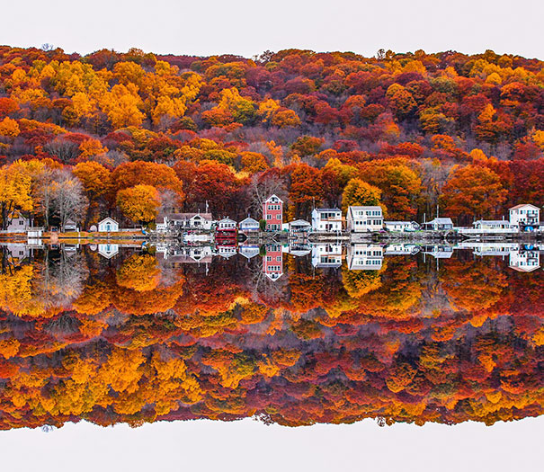 Charming reflection of colorful autumn trees and houses on a calm lake, capturing a perfectionist's soul.