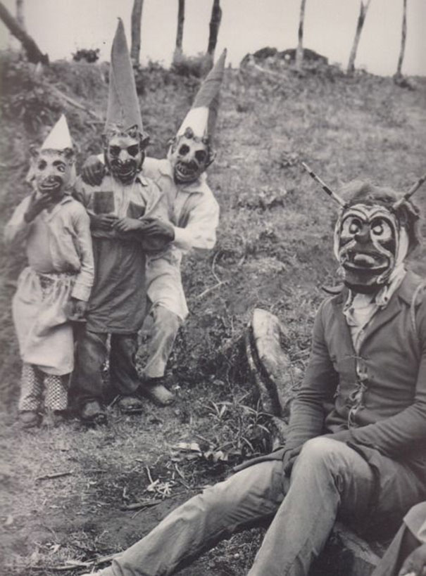 Group of people wearing vintage Halloween costumes with creepy masks and pointed hats in an outdoor setting.