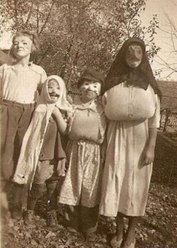 Children in vintage Halloween costumes posing outdoors with homemade masks and outfits in an old black and white photo