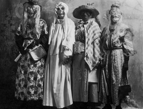 Four people wearing vintage Halloween costumes including masks and long dresses, showcasing classic spooky style.