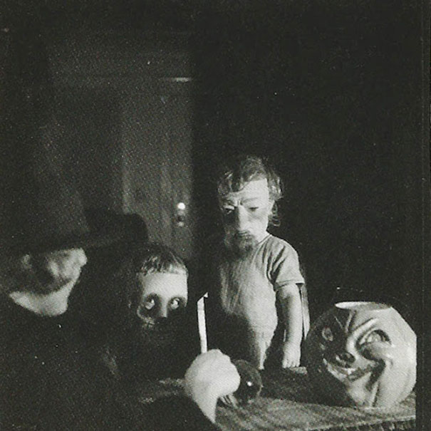 Vintage Halloween costumes featuring eerie masks and figures gathered around a table in a dimly lit setting.
