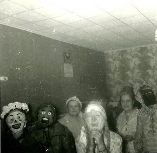 Group of people in vintage Halloween costumes with eerie makeup posing indoors, showcasing classic spooky Halloween style.
