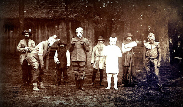 Group of children and adults wearing vintage Halloween costumes in a sepia-toned outdoor setting, showcasing spooky styles.