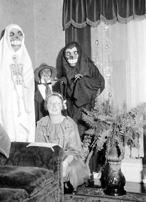 Vintage Halloween costumes featuring skeleton masks and spooky outfits in a historic black and white indoor setting.