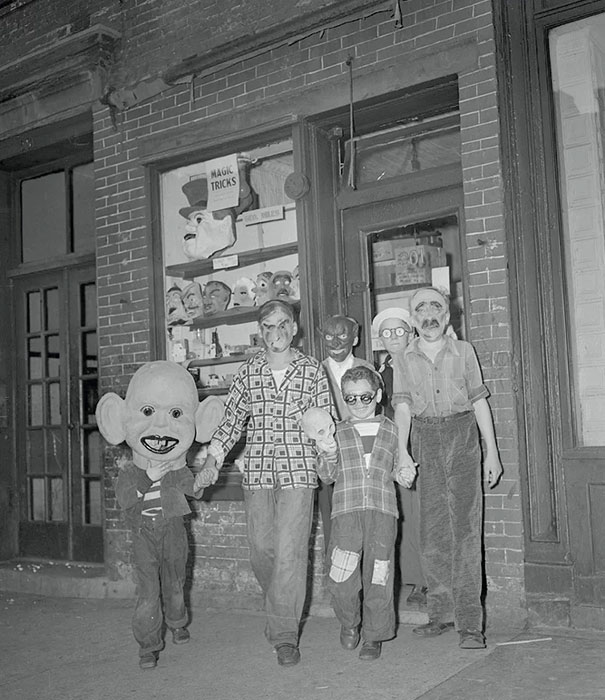 Group of children wearing scary vintage Halloween costumes and masks standing outside a brick building at night