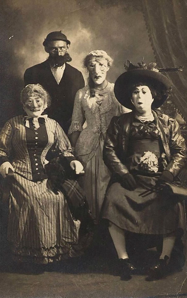 Vintage Halloween costumes featuring eerie masks and period clothing in a black and white spooky group portrait.