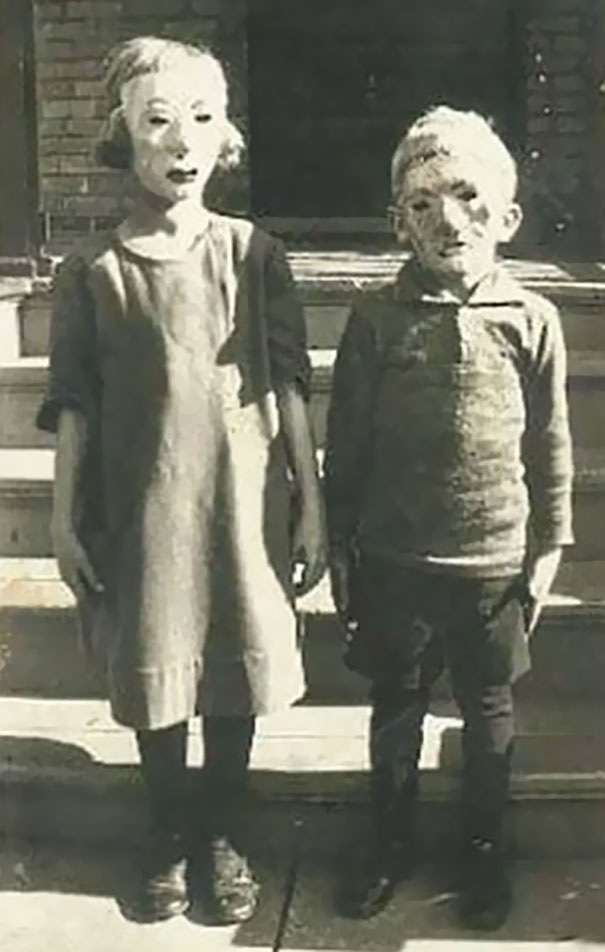 Two children wearing vintage Halloween costumes with eerie masks standing on outdoor steps in black and white photo