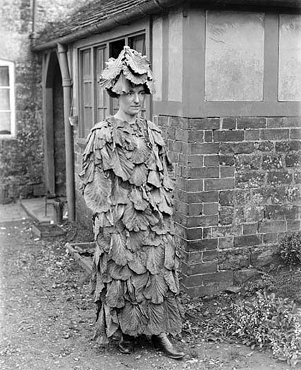 Woman wearing a vintage Halloween costume made of large leaves and a matching leafy hat standing by a brick building.