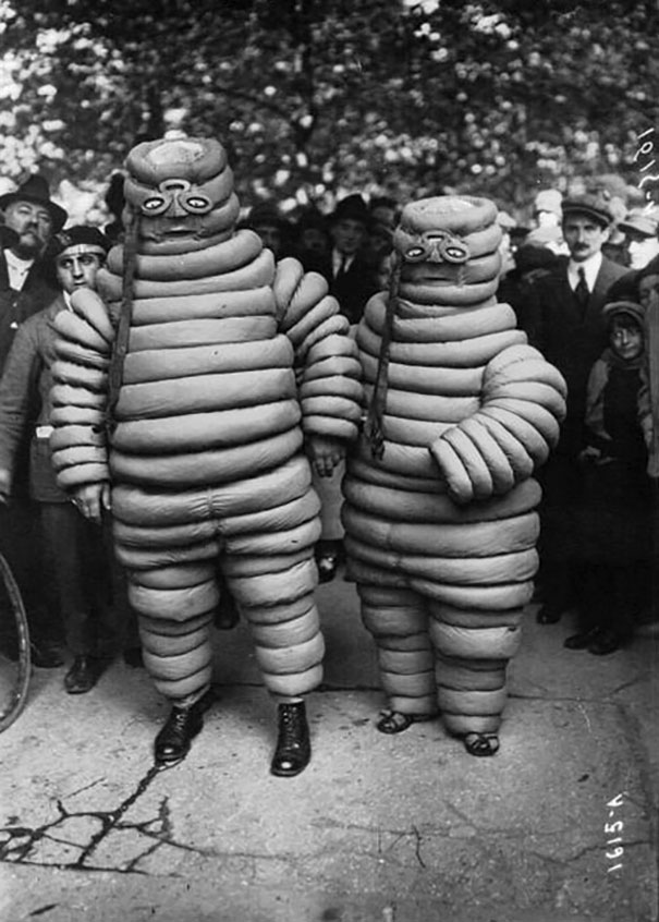 Two people wearing vintage Halloween costumes resembling coiled tubes, surrounded by onlookers outdoors.