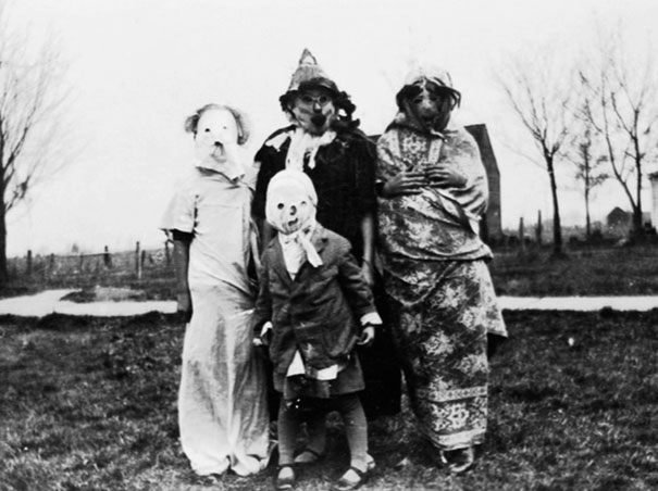 Group of children wearing vintage Halloween costumes with eerie masks posing outdoors on a gloomy day.