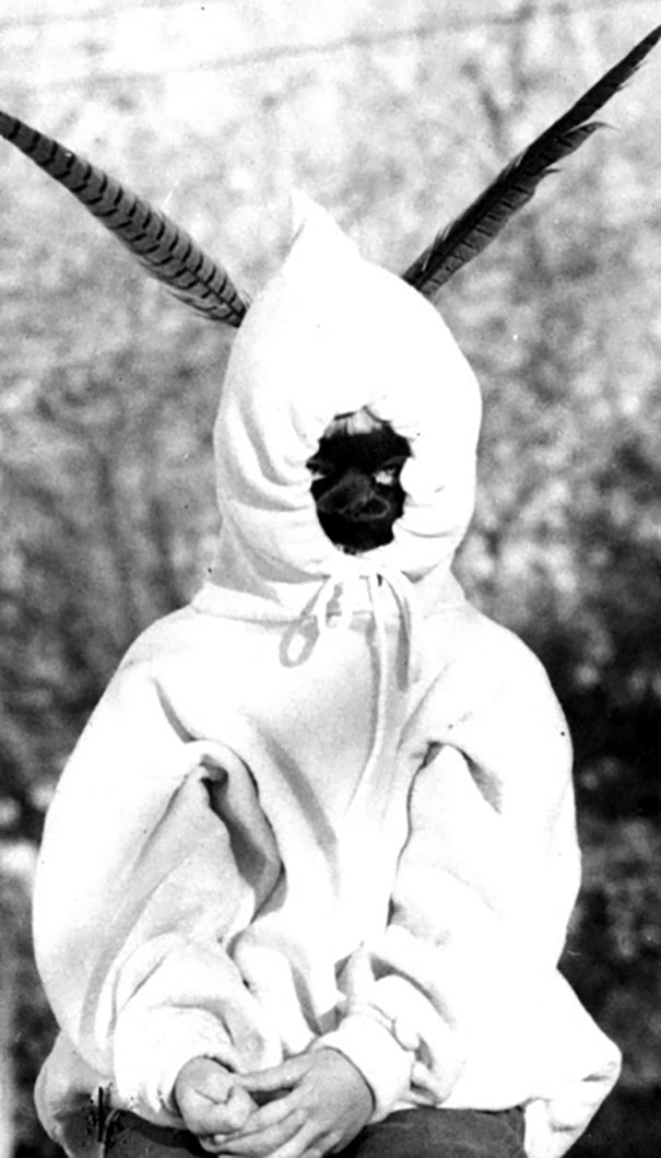 Child in a vintage Halloween costume with a hood and feather antennae sitting outdoors in black and white.