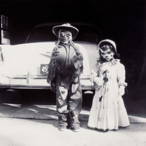 Two children in vintage Halloween costumes standing in front of a classic car, showcasing spooky retro Halloween style.