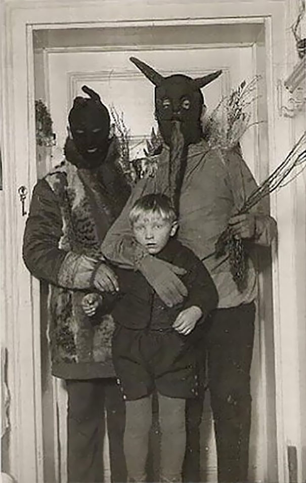 Two adults in vintage Halloween costumes wearing masks, holding a young boy, showcasing vintage Halloween costumes.