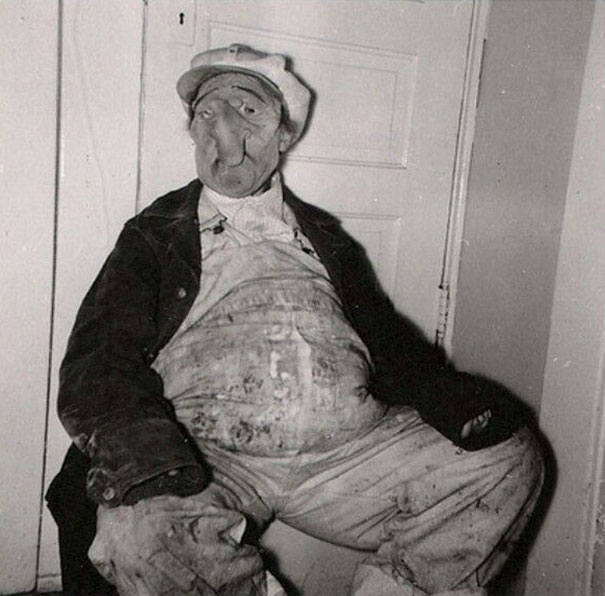 Vintage Halloween costume featuring a creepy mask and worn clothing sitting against a door in black and white.