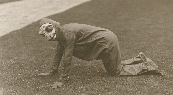Person in a creepy vintage Halloween costume crawling on grass, showcasing early spooky costume design.
