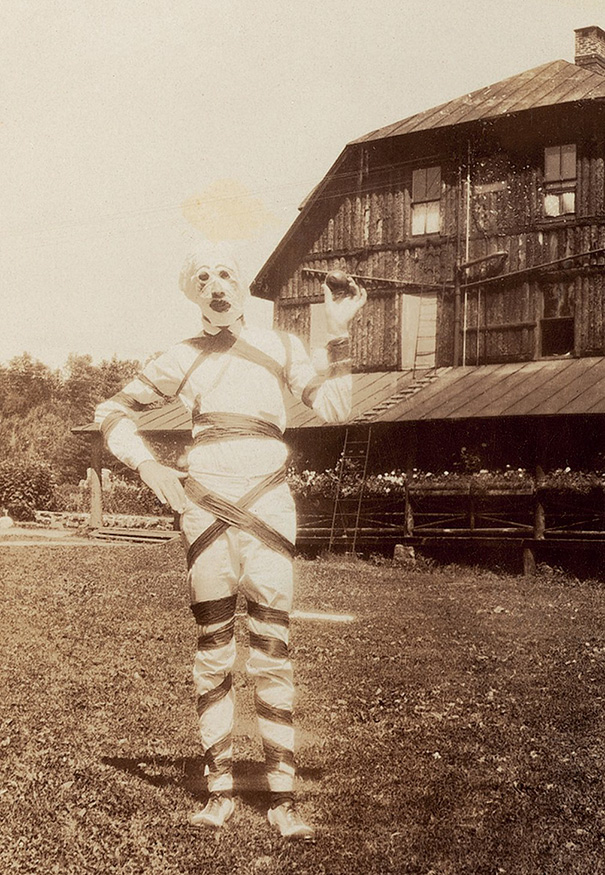 Vintage Halloween costume resembling a mummy with wrapped bandages standing outdoors near a rustic wooden house.