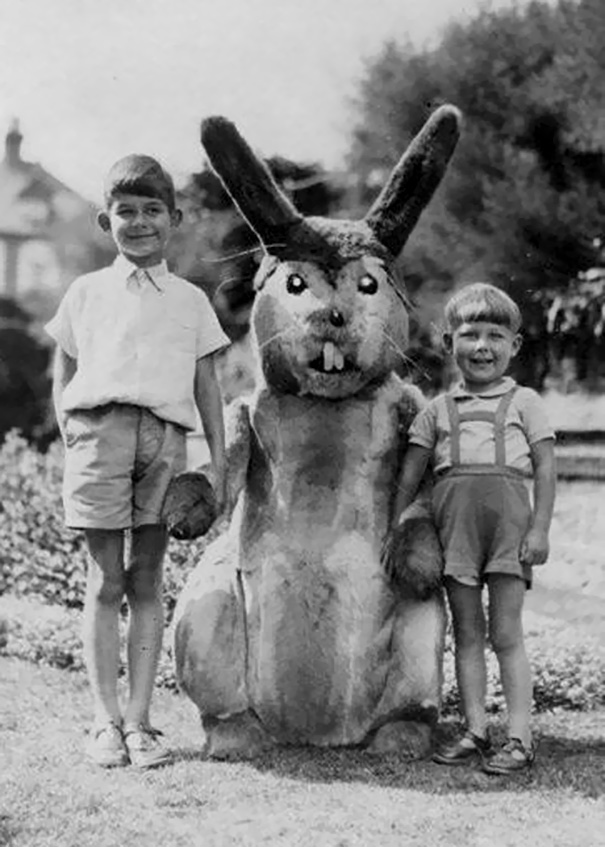 Two boys standing outside with a person in a vintage Halloween costume of a large, scary rabbit.