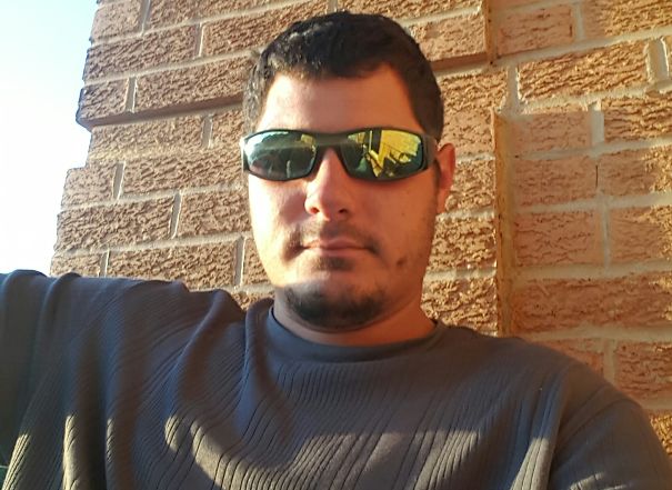 Man wearing dark sunglasses and a gray shirt sitting against a brick wall showing effects of stopping drinking.