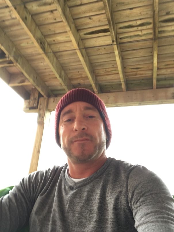 Man wearing a red beanie and gray shirt taking a selfie under a wooden roof, showing changes after stopping drinking.
