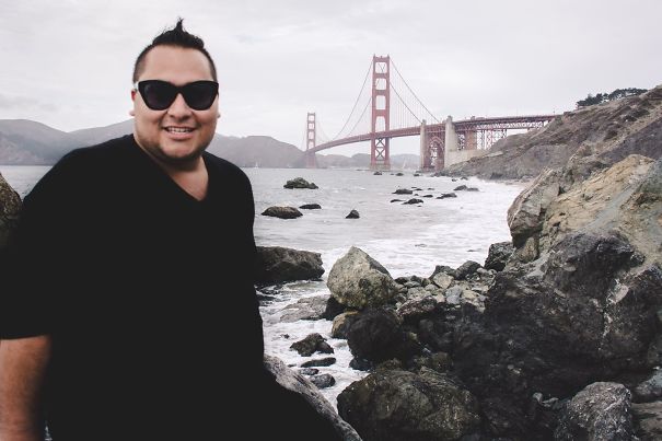 Man wearing sunglasses smiling by rocky shore with Golden Gate Bridge in background, illustrating before and after quitting drinking effects