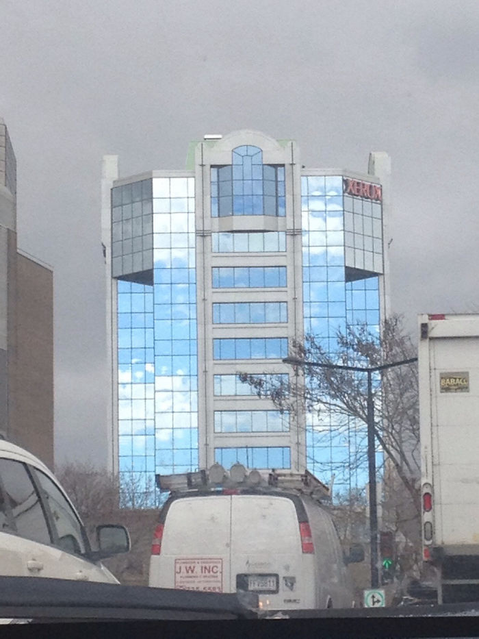 Behind This Building Is Grey And Gloomy, But The Reflection In The Building Is Bright And Blue