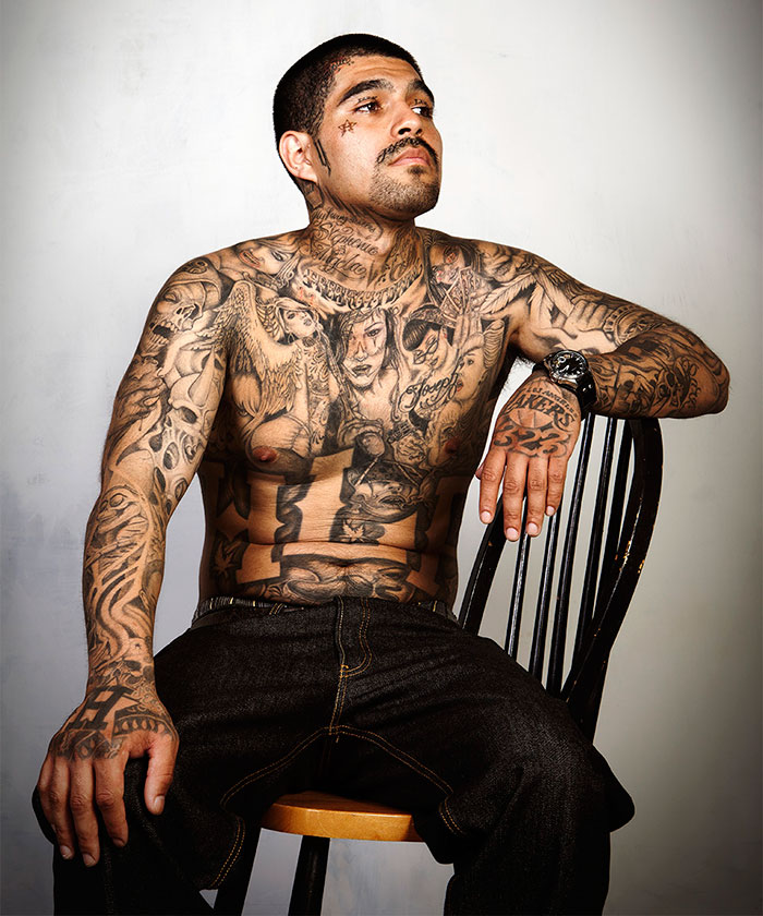 Ex-gang member with tattoos sitting on a chair, symbolizing a change in lifestyle and identity. Ex-gang member with tattoos sitting on a chair, symbolizing a change in lifestyle and identity.