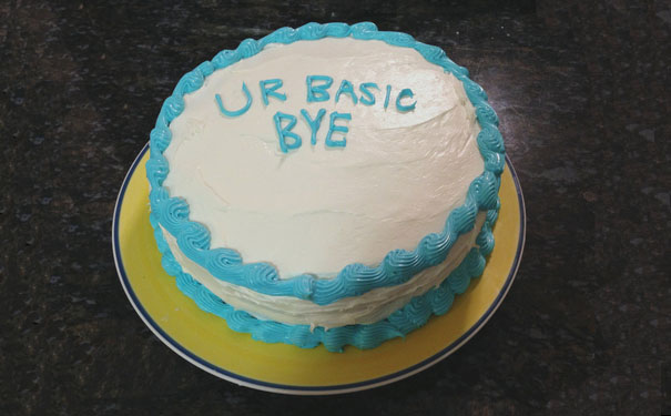 Farewell cake with blue icing that reads "UR BASIC BYE" on a dark surface.