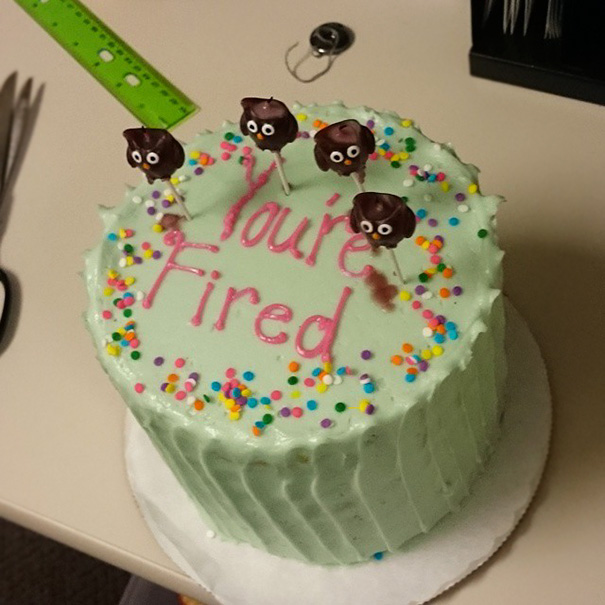Farewell cake with "You're Fired" text, decorated with colorful sprinkles and amusing chocolate figures.