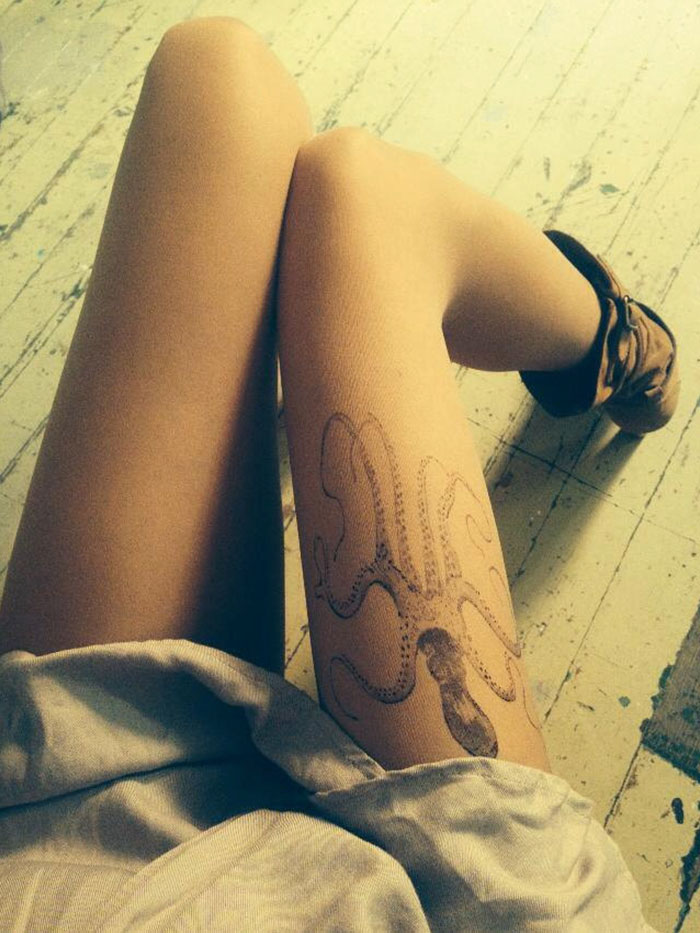 Tattoo tights with an octopus design, creating an illusion of inked legs, worn by someone seated on a wooden floor.