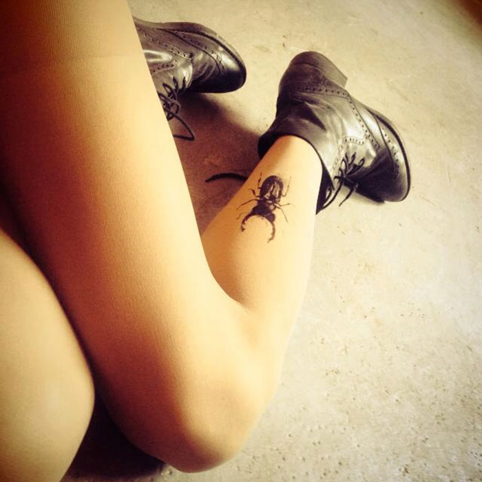 Legs in tattoo tights with bug design, creating an inked illusion, paired with black shoes on a concrete floor.