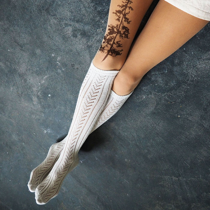 Legs wearing tattoo tights with tree design creating illusion of inked skin on a textured surface.
