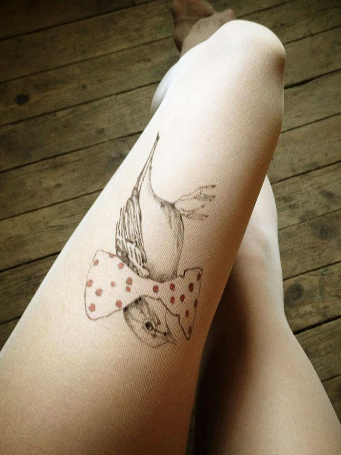 Tattoo tights with bird and bow design create illusion of inked leg on wooden floor background.