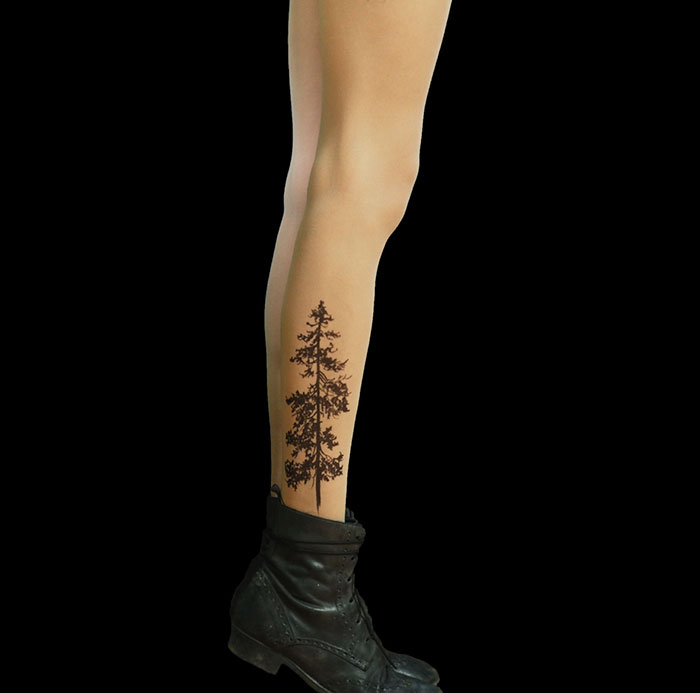 Leg wearing tattoo tights with tree design, creating an inked illusion, paired with black boots.