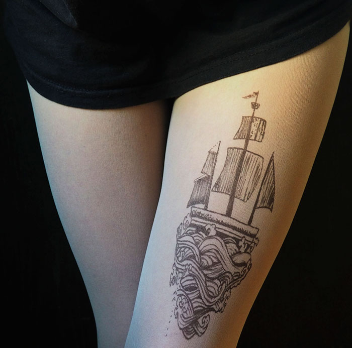 Tattoo tights creating an illusion of a ship tattoo on a woman's leg against a black background.