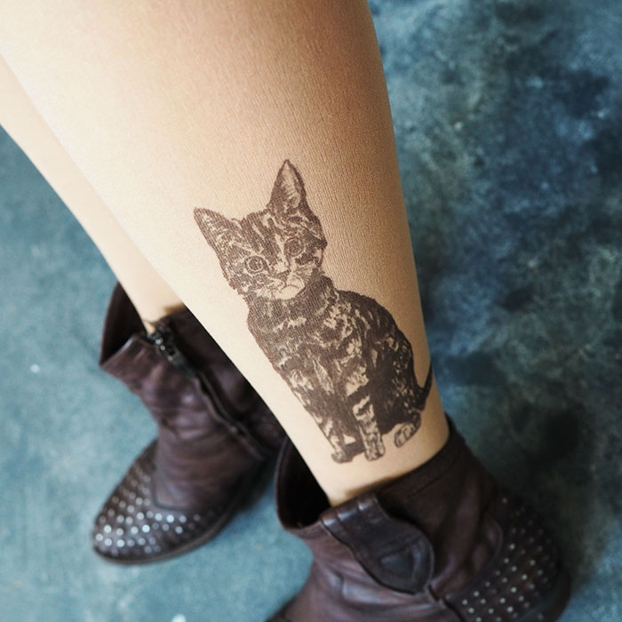Tattoo tights with a cat design creating an inked illusion on legs, paired with studded brown boots.
