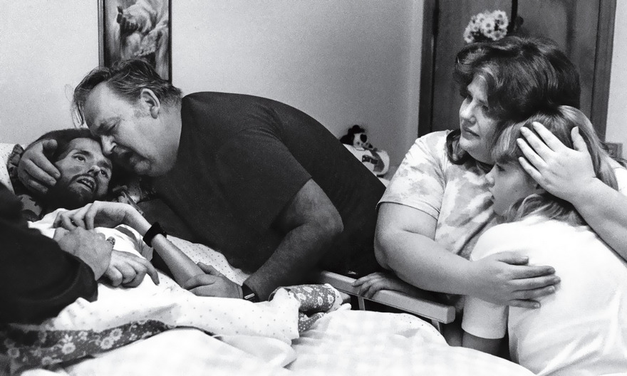 Family shares an emotional moment with a loved one in a hospital bed, capturing a historically famous photo.