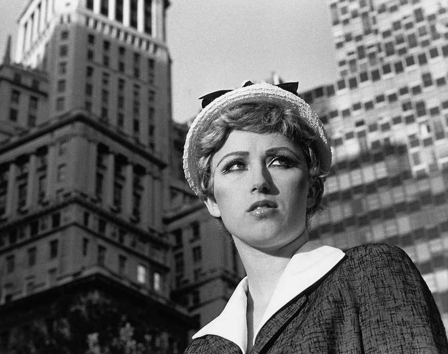 A woman in vintage clothing poses against skyscrapers, capturing an iconic moment in history.