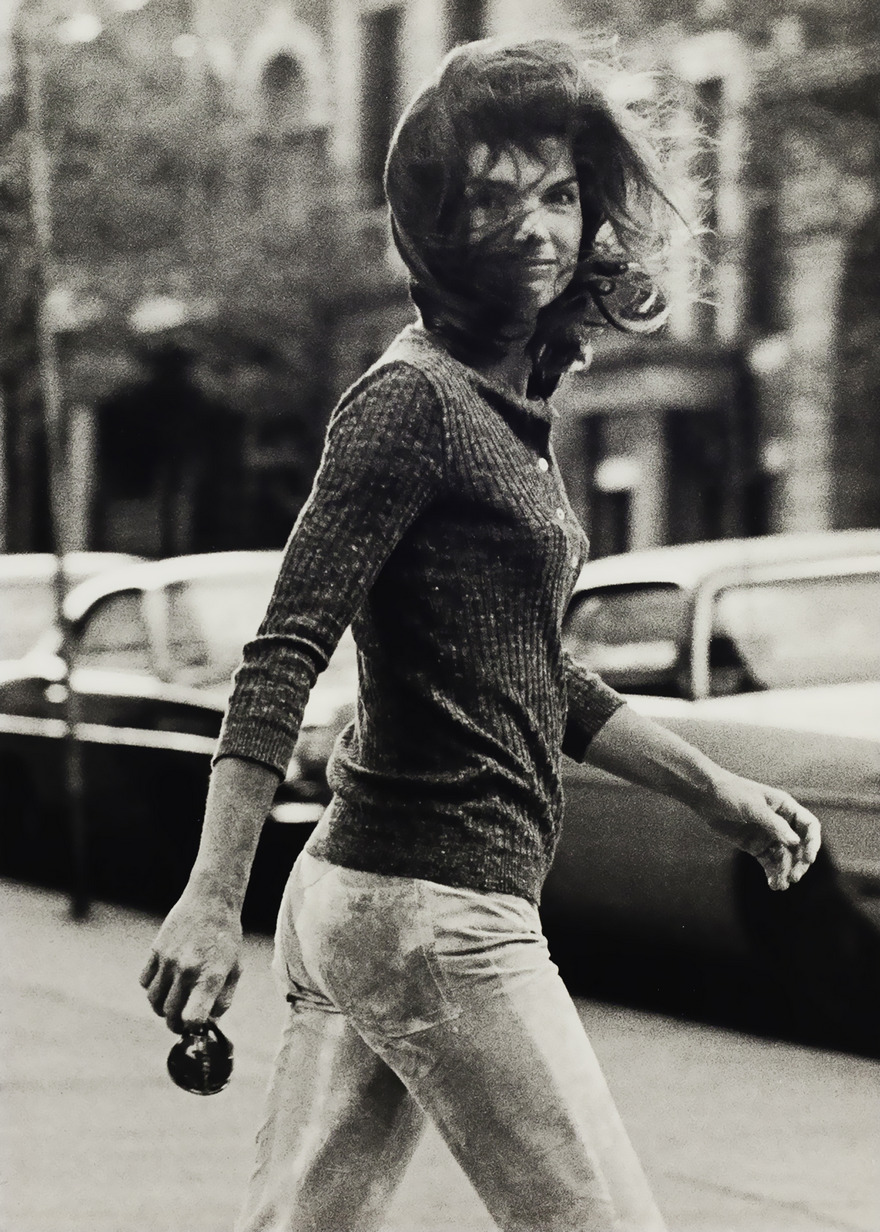 Woman walking confidently on a city street, captured in a classic black and white photograph.