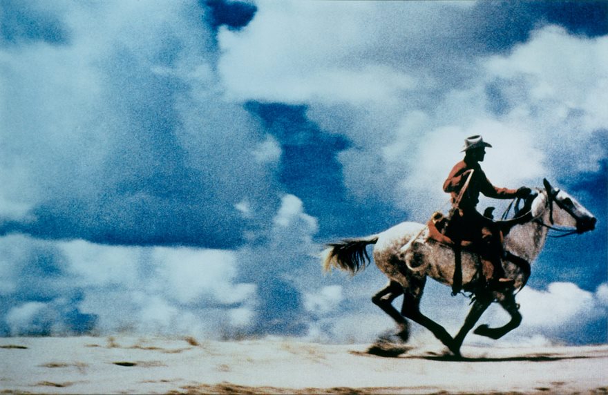 Cowboy riding a horse across a desert landscape under a dramatic sky, from famous photos in history.