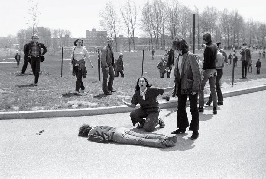 Historic protest scene with individuals reacting emotionally around a fallen person on a university campus.