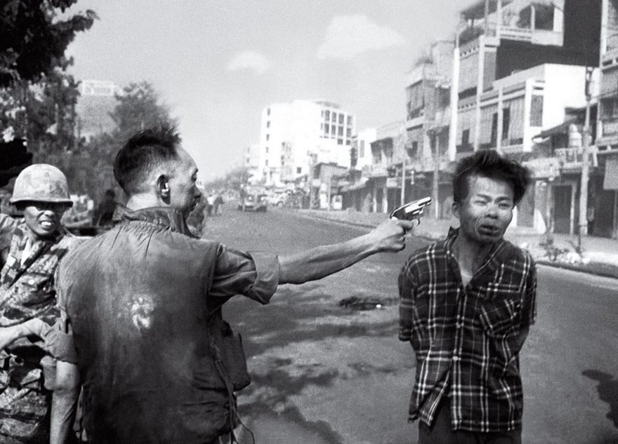A soldier aiming a gun at a man's head on a city street; iconic historical photo capturing a tense moment.